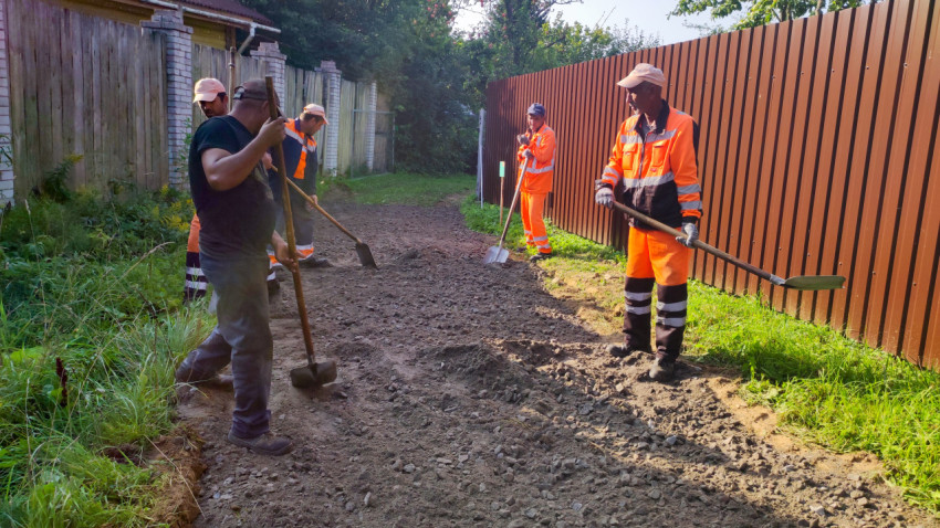 Рабочие в сигнальных жилетах выполняют ремонт грунтовой дороги ручным инструментом