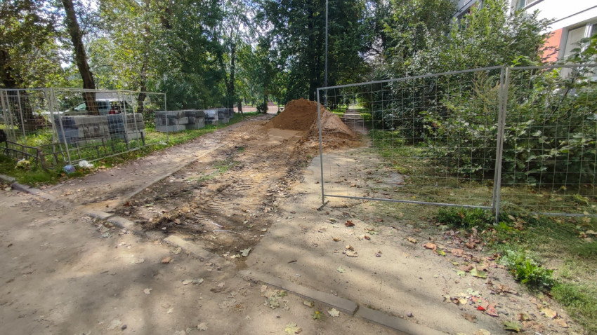 Временные секции забора и куча песка перекрывают дорожку в зелёном дворе