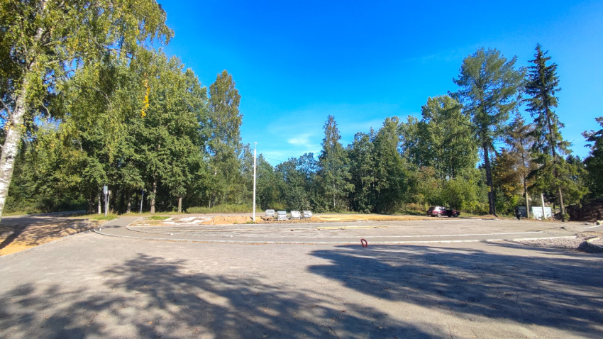 Новая асфальтовая площадка у леса с бордюрами и стопками плитки