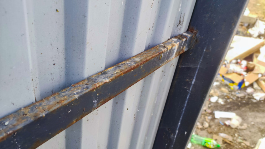 Крупный план ржавой поперечины металлического забора на фоне профнастила