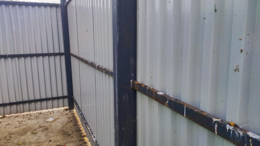 Угол ограждения из профнастила с металлическим каркасом и следами ржавчины на бетоне