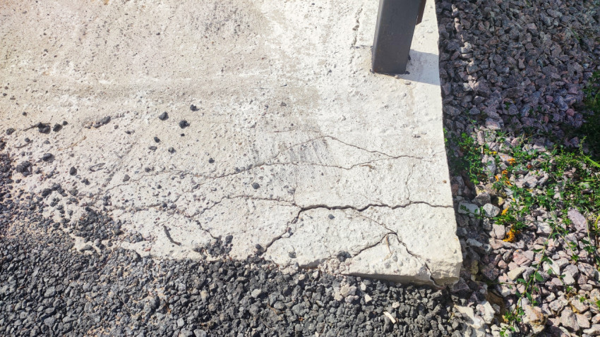 Трещины и сколы на кромке бетонной плиты у основания металлической стойки