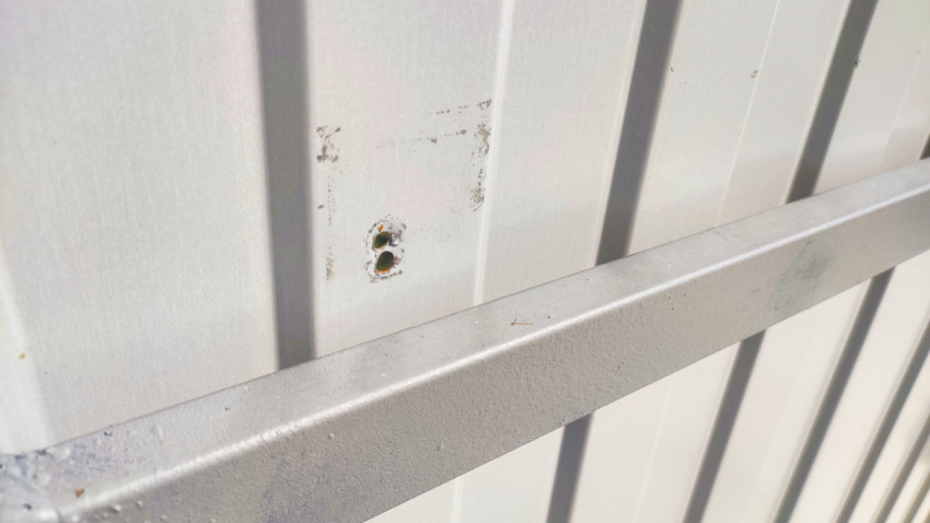 Два отверстия и сколы краски на панели ограждения контейнерной площадки рядом с поперечной балкой