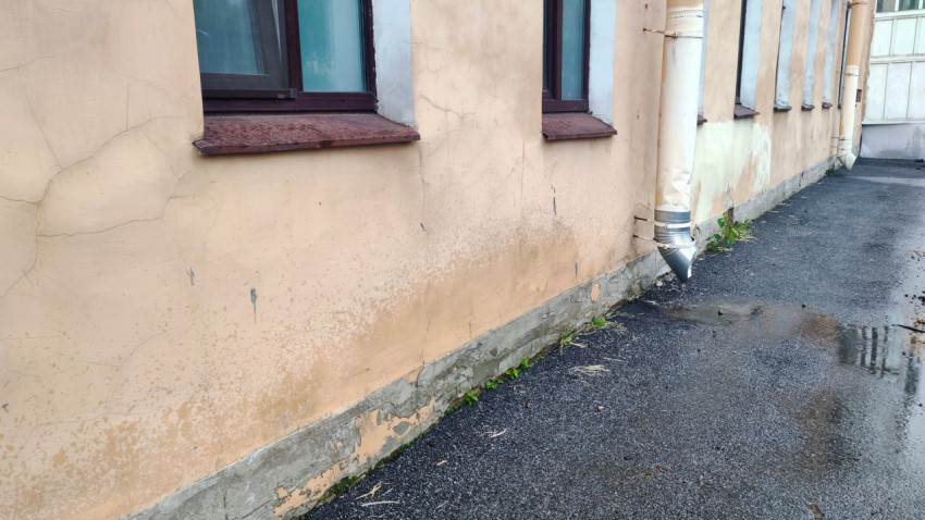 Водосточная труба у фасада жилого дома с мокрым пятном и лужами на асфальте