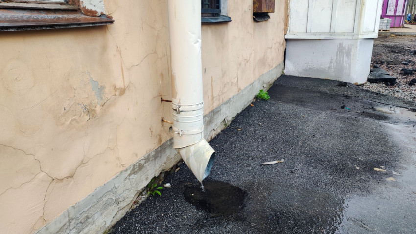 Повреждённая штукатурка цоколя и следы сырости у основания стены рядом с влажным дворовым покрытием
