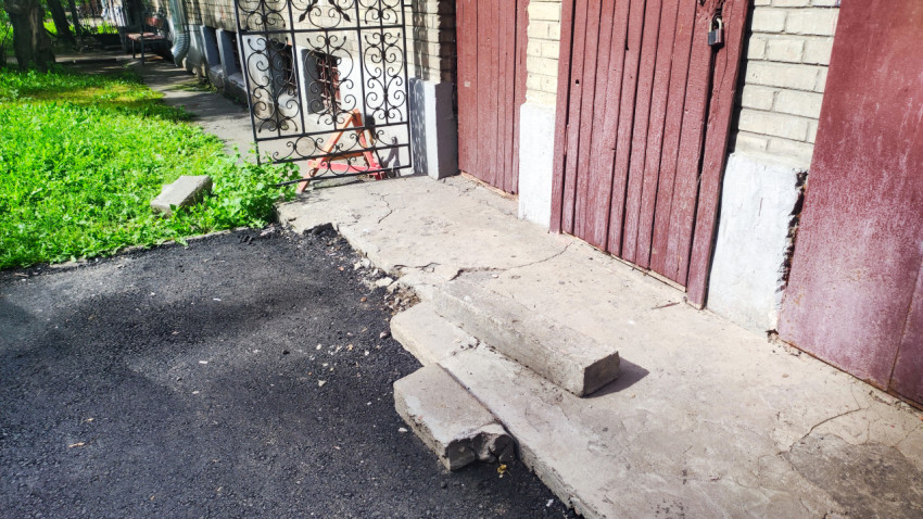 Свежий асфальт и бордюр у входной зоны кирпичного дома с бетонными ступенями и металлическими дверями