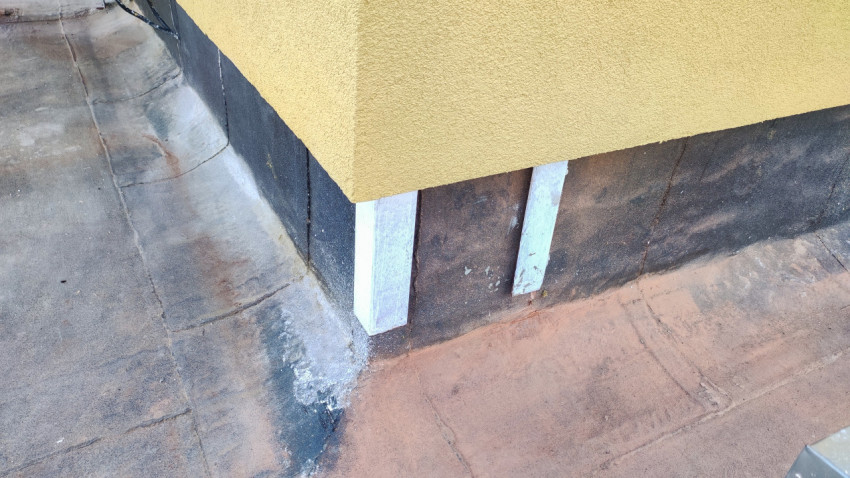 Угол парапета на плоской кровле с рулонной гидроизоляцией и следами ремонта у стены