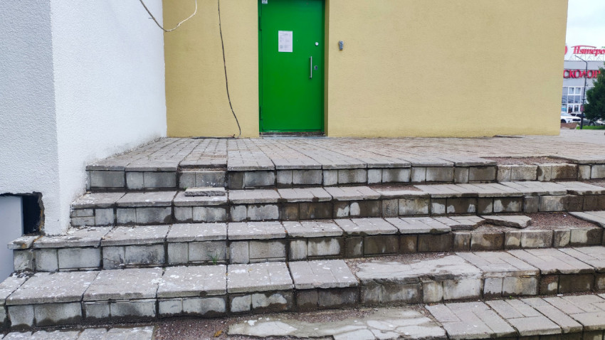 Изношенные бетонные ступени и зеленая металлическая дверь входной группы здания