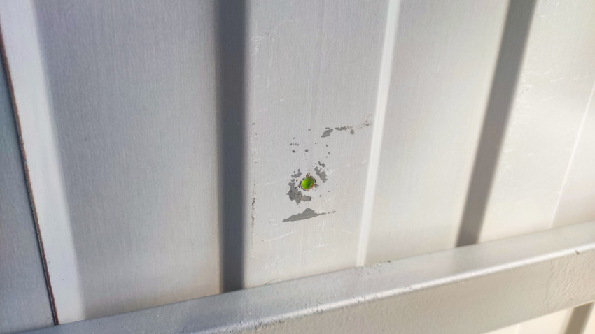 Сколы покрытия вокруг отверстия крепежа на панели ограждения контейнерной площадки крупным планом