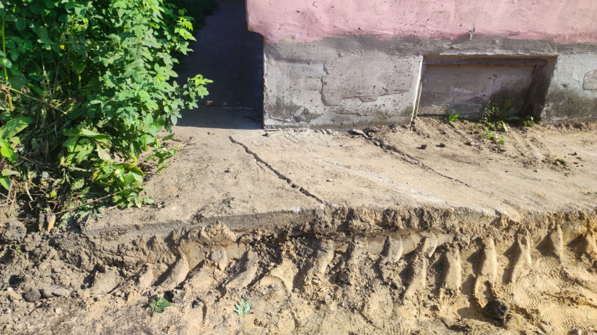 Повреждённая штукатурка и трещины на бетонном цоколе жилого дома рядом с земляной насыпью