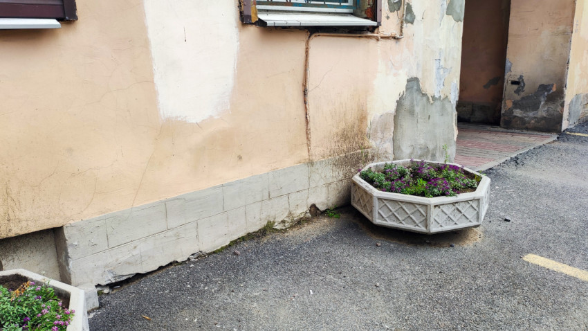 Трещины и потёки на стене дома возле входной арки и уличных вазонов с цветами