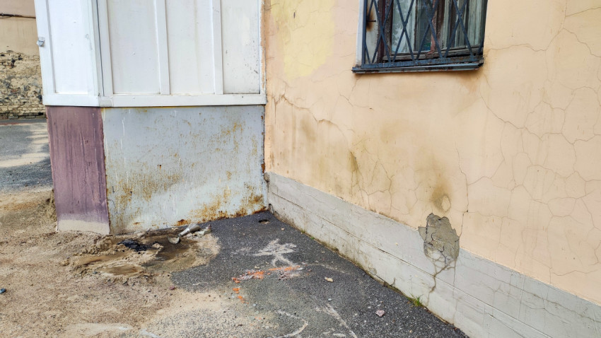 Угол фасада и цоколя многоквартирного дома с осыпающейся отделкой и трещинами у придомового покрытия