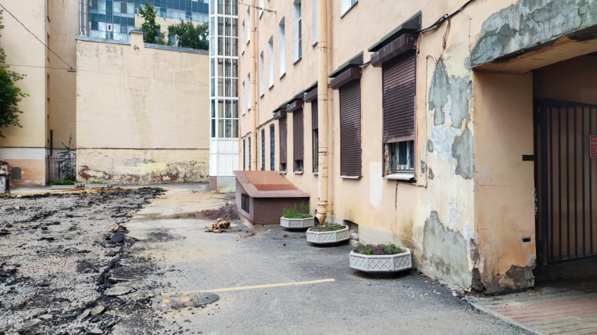Разрушенная отмостка и отслаивающаяся штукатурка на фасаде жилого дома у тротуара