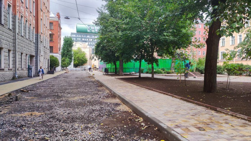 Снятый асфальт и новый тротуар из плитки вдоль двора с деревьями