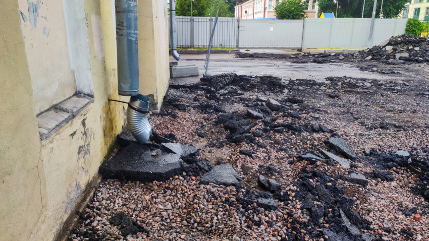 Разобранное асфальтовое покрытие у стены здания с водосточной трубой