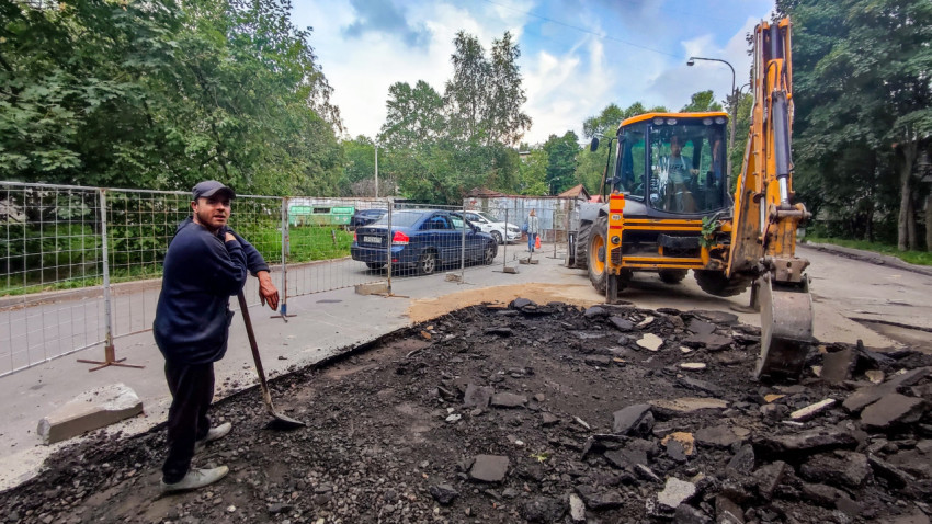 Рабочие и экскаватор-погрузчик на участке фрезерования асфальта во дворе жилого квартала