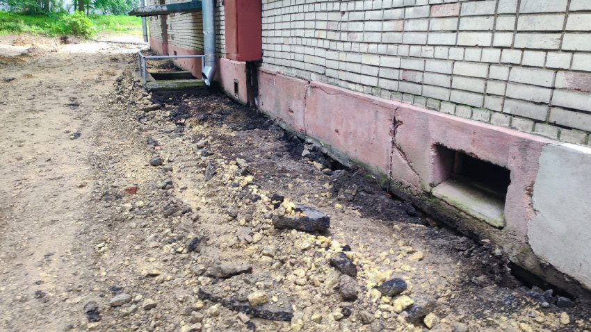 Раскопка вдоль фундамента кирпичного дома с щебнем и строительным мусором