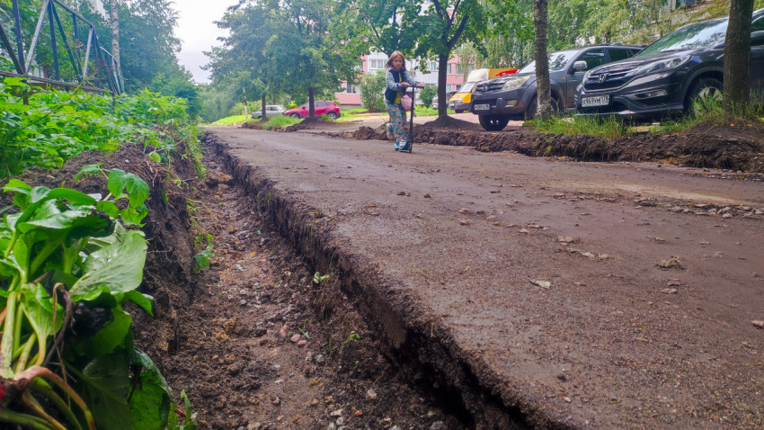 Девочка на самокате едет по дворовой дороге с вырезанной кромкой асфальта