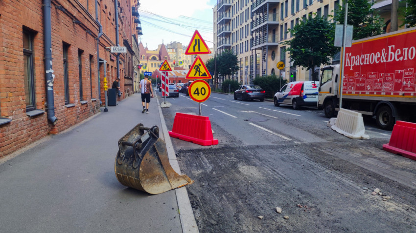 Ремонт проезжей части с ковшом экскаватора, ограждениями и временными дорожными знаками на городской улице