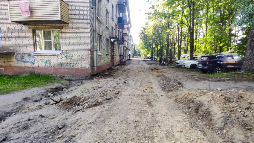 Внутридворовой проезд после снятия асфальта рядом с припаркованными автомобилями и деревьями