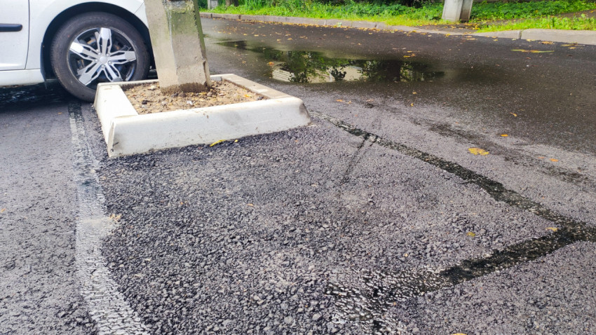 Неровный стык асфальта вокруг бетонного основания опоры и лужа на дворовой дороге