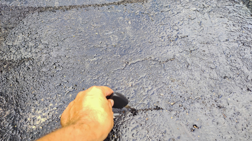 Рука с ключом показывает глубокий разлом на асфальтовом покрытии возле шва ремонта