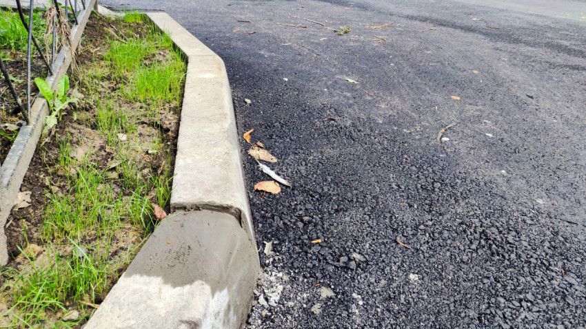 Кромка асфальта у бордюра с гравием и следами незавершённых работ на дворовой территории