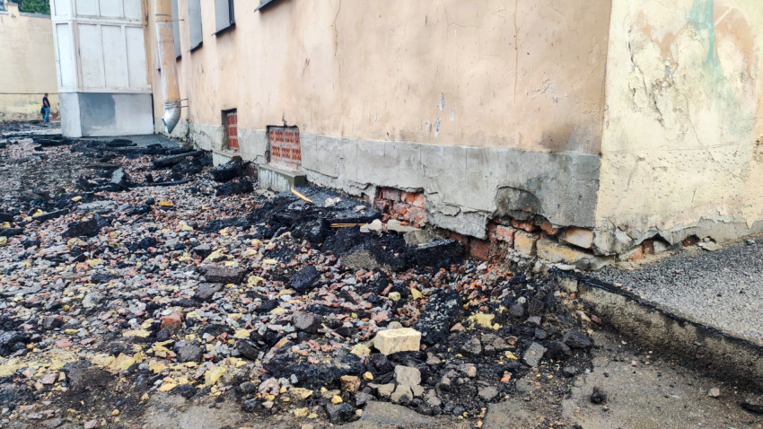 Повреждённый цоколь с открытой кирпичной кладкой и россыпью строительных обломков вдоль стены