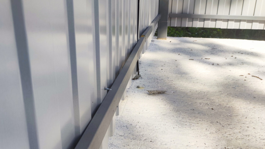 Нижняя балка ограждения контейнерной площадки с выступающим крепежом над бетонной плитой