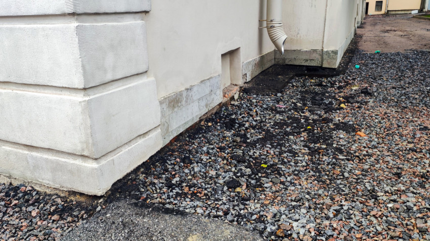 Белый фасад с цоколем, вентиляционным отверстием и водосточной трубой на гравийной отсыпке