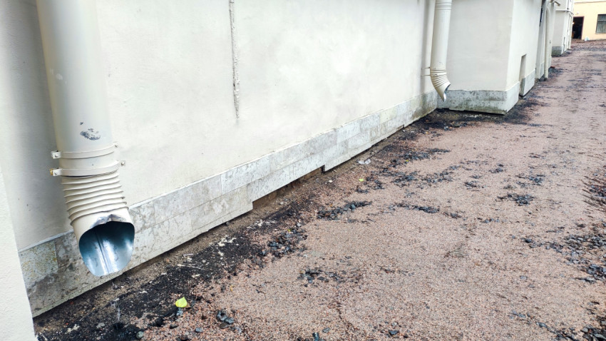 Водосточная труба со сливом в гофрированный отвод у цоколя жилого дома