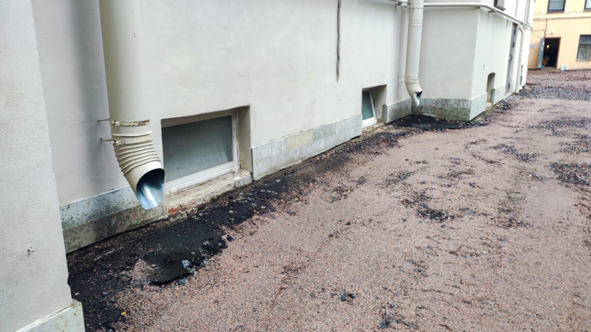 Водосточный стояк рядом с подвальным окном и щебёночной отсыпкой у фундамента