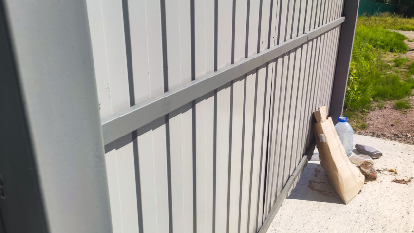 Ограждение контейнерной площадки из серого профлиста рядом с картоном и пластиковой тарой на бетонном основании