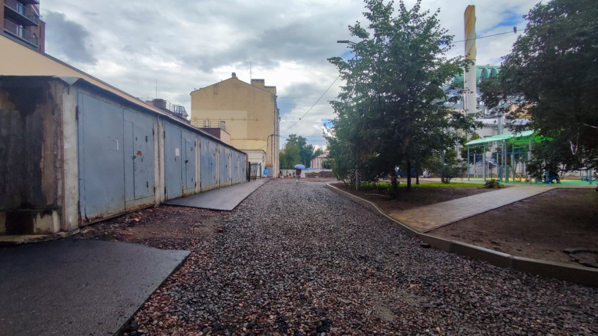 Ряд металлических гаражей и гравийный проезд во дворе рядом с детской площадкой