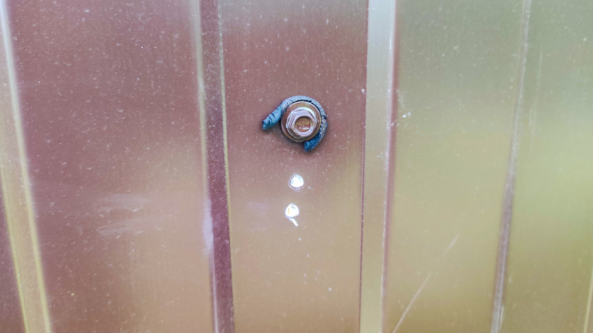 Крепёжный болт на металлическом профлисте с следами герметика