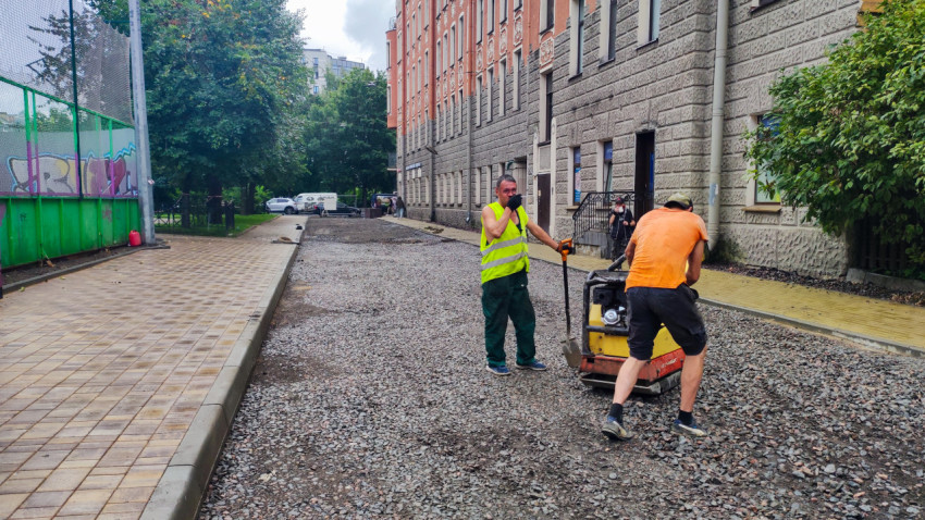 Рабочие уплотняют щебёночное основание виброплитой во дворе жилого дома