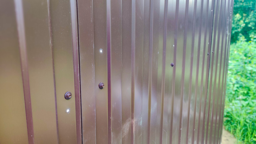 Фрагмент забора из профнастила с рядом крепёжных болтов на улице