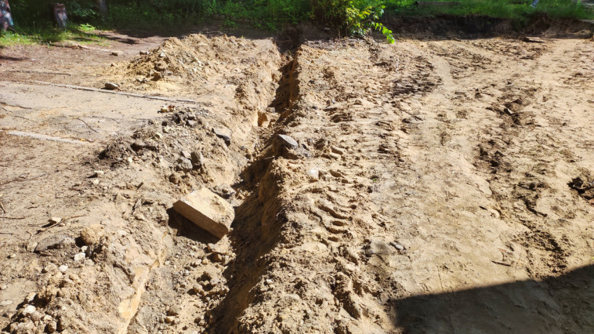 Крупный план траншеи с песчано-глинистым грунтом, камнями и колеями от техники