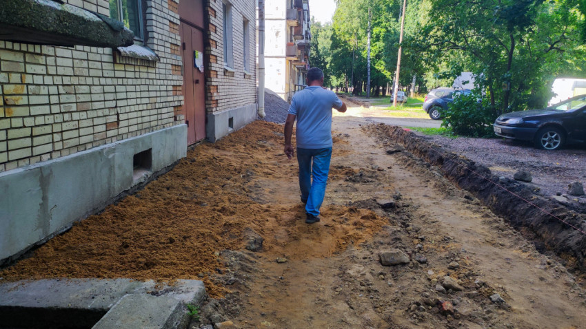 Раскопки у фасада дома с разметкой, песком и пешеходом на дворовом проходе