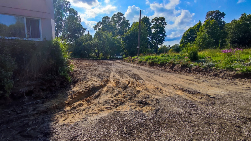 Утрамбованный грунтовый проезд со щебнем и колеями в жилом дворе под облачным небом
