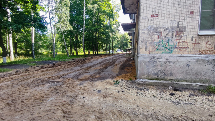 Грунтовый проезд после снятия асфальта у торца дома с колеями и кромкой песчаной насыпи