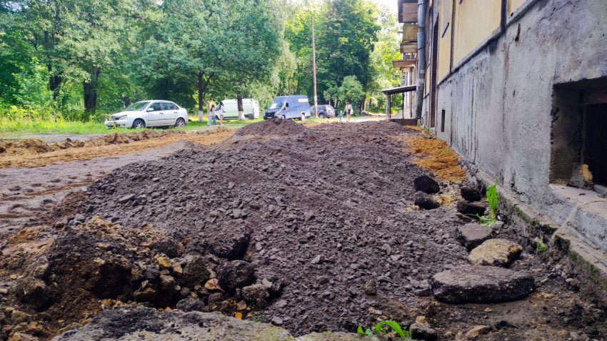 Куча асфальтовой крошки и грунта у стены дома на участке ремонта дворового проезда