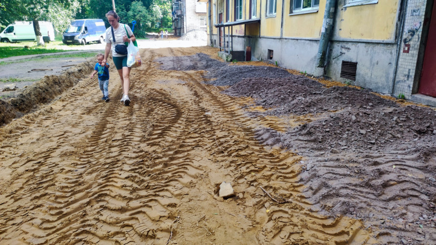 Женщина и ребёнок идут по ремонтируемому дворовому проезду с песком и асфальтовой крошкой