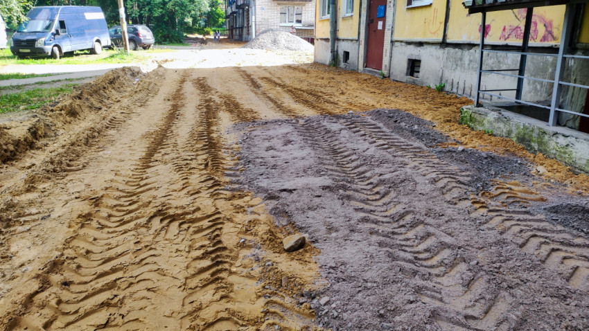 Песчаное основание и полоса асфальтовой крошки на дворовой дороге у дома после демонтажа покрытия
