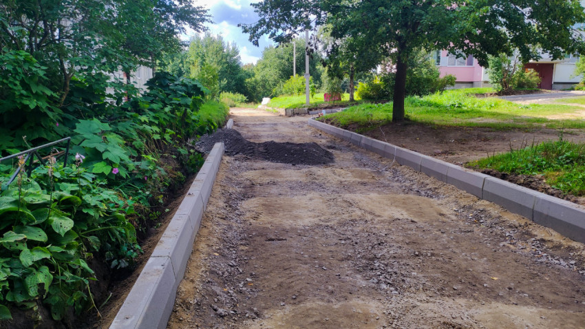 Подготовленное основание дороги между бордюрами с насыпями грунта и щебня в зелёной зоне двора