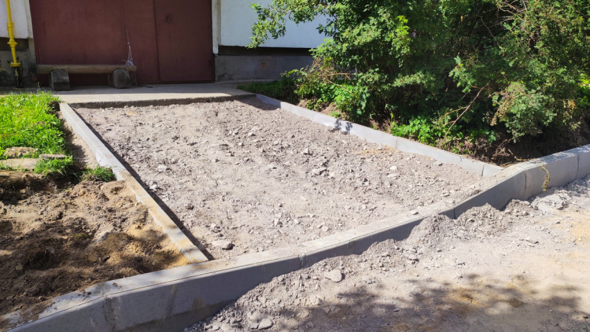 Щебёночная подсыпка в ограниченном бордюрами проезде у подъезда жилого дома перед укладкой покрытия