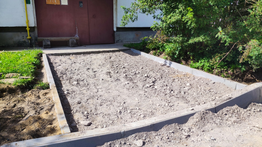 Участок у подъезда с уложенными бордюрами и щебёночной подсыпкой, подготовленный под тротуарное покрытие