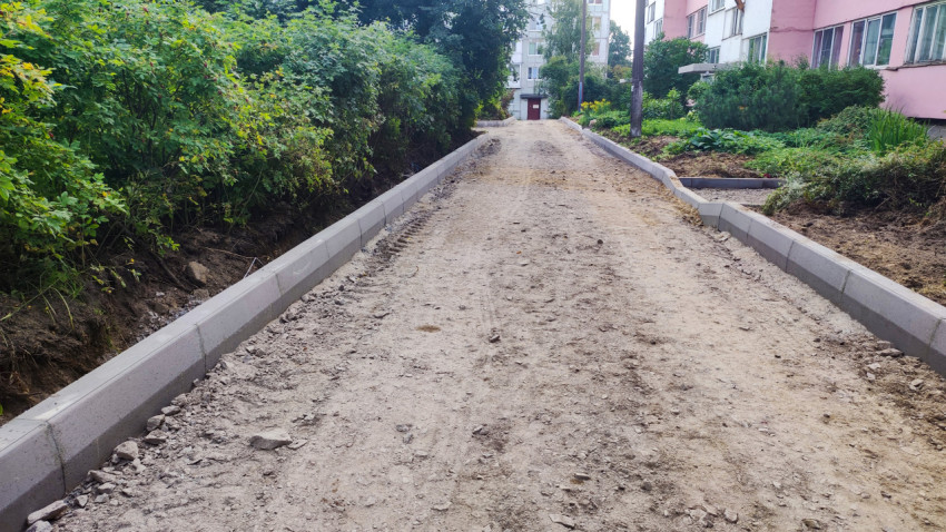 Песчано-щебёночное основание будущей дороги между бордюрами в жилом квартале рядом с зелёными насаждениями