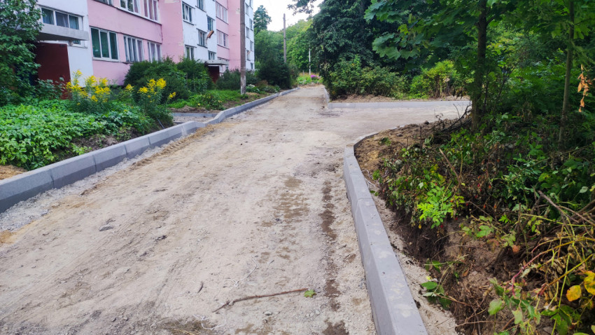 Дворовой проезд в ремонте с щебёночным основанием, бордюрами и жилыми домами на фоне