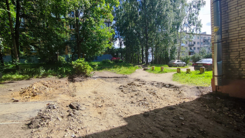 Разрушенное покрытие во дворе с грунтом и щебнем между деревьями и жилыми домами